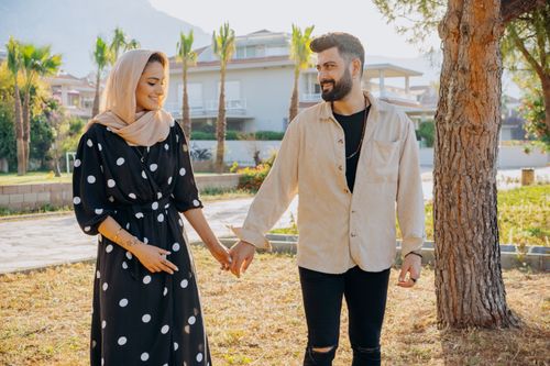 Free A happy couple holding hands and walking outdoors, enjoying a sunny summer day. Stock Photo