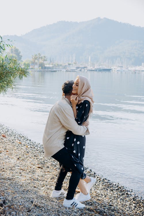 Free Woman in White Coat Kissing Man in Black and White Polka Dot Jacket on Beach during Stock Photo