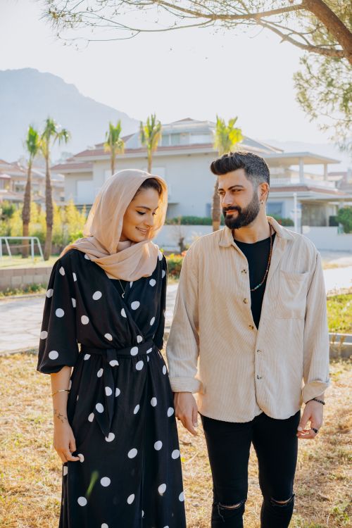 Free A stylish couple walking in a sunlit park, dressed fashionably with polka dot dress and headscarf. Stock Photo