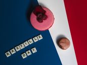 Artistic flat lay of Bastille Day celebration with macarons and Scrabble tiles spelling Bastille on tricolor background.