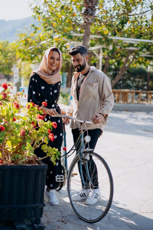 Free A joyful couple smiles beside a bicycle outdoors in a bright park setting. Stock Photo