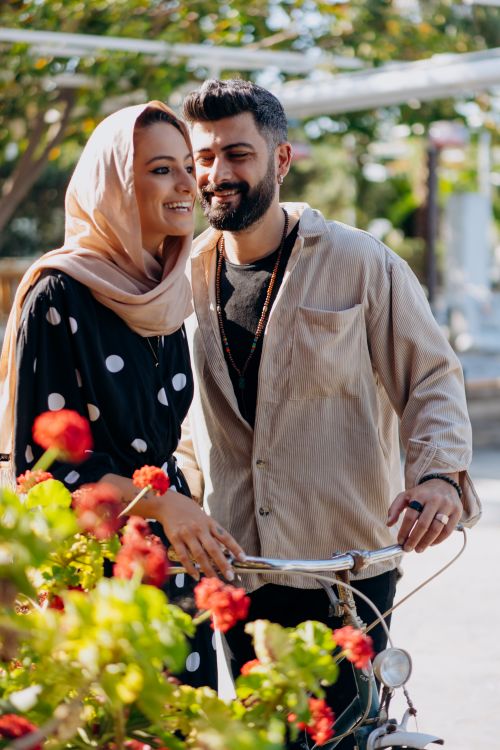 Free Smiling couple with bicycle in a sunny park, surrounded by vibrant flowers. Stock Photo
