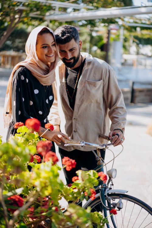 Free Happy couple walking with bicycle surrounded by flowers on a sunny day Stock Photo