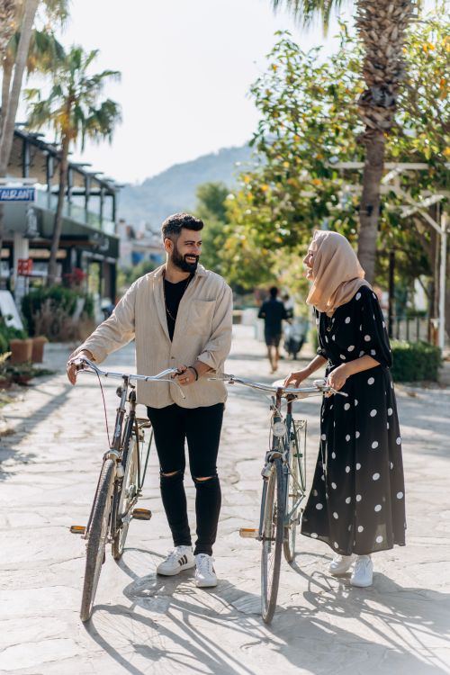 Free A smiling couple walking with bicycles along a sunny path, enjoying a casual outing. Stock Photo