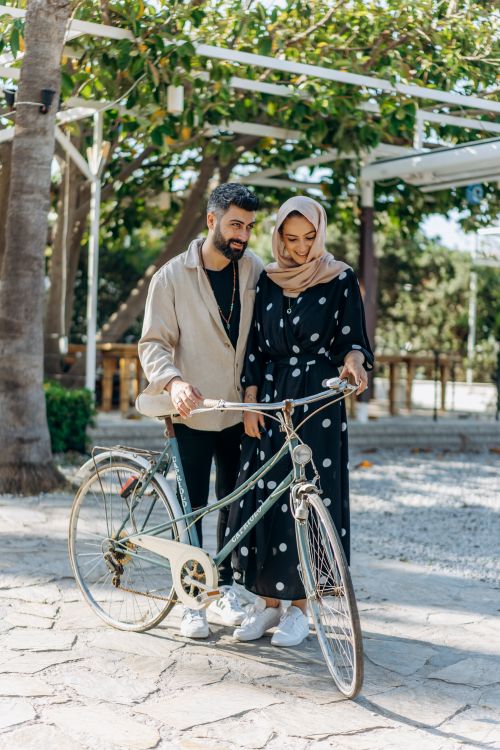 Free A joyful couple standing beside a vintage bicycle in a sunny park, sharing a moment of connection. Stock Photo
