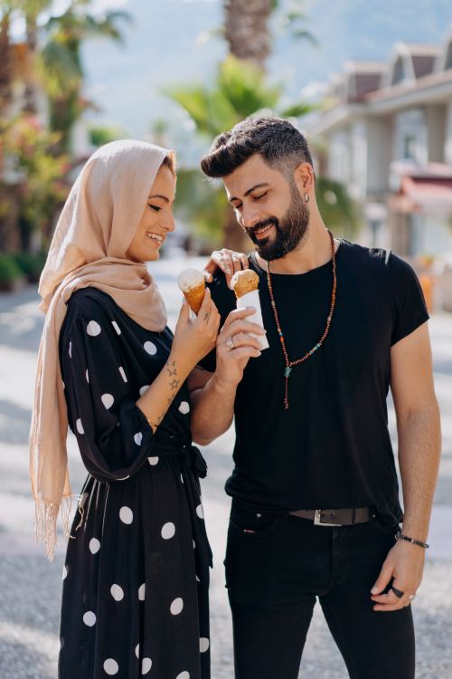 Free Smiling couple with ice cream in a sunny street, sharing a joyful moment. Stock Photo