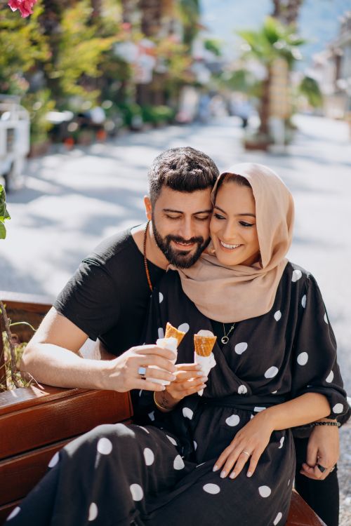 Free A happy couple sitting on a bench enjoying ice cream cones in a sunny outdoor setting. Stock Photo