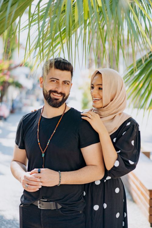 Free Smiling couple embracing under palm leaves on a sunny day, enjoying each other's company. Stock Photo