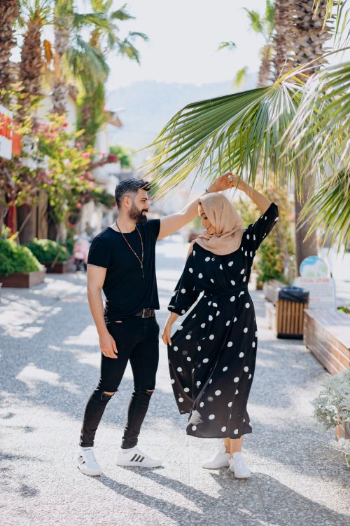 Free Stylish couple holding hands under palm trees in a sunny outdoor location. Stock Photo