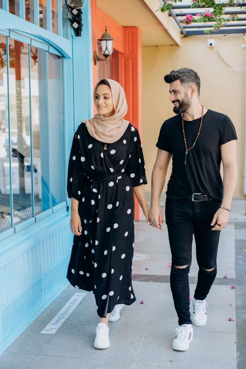 Free A fashionable couple holding hands and walking outside a colorful building. Stock Photo
