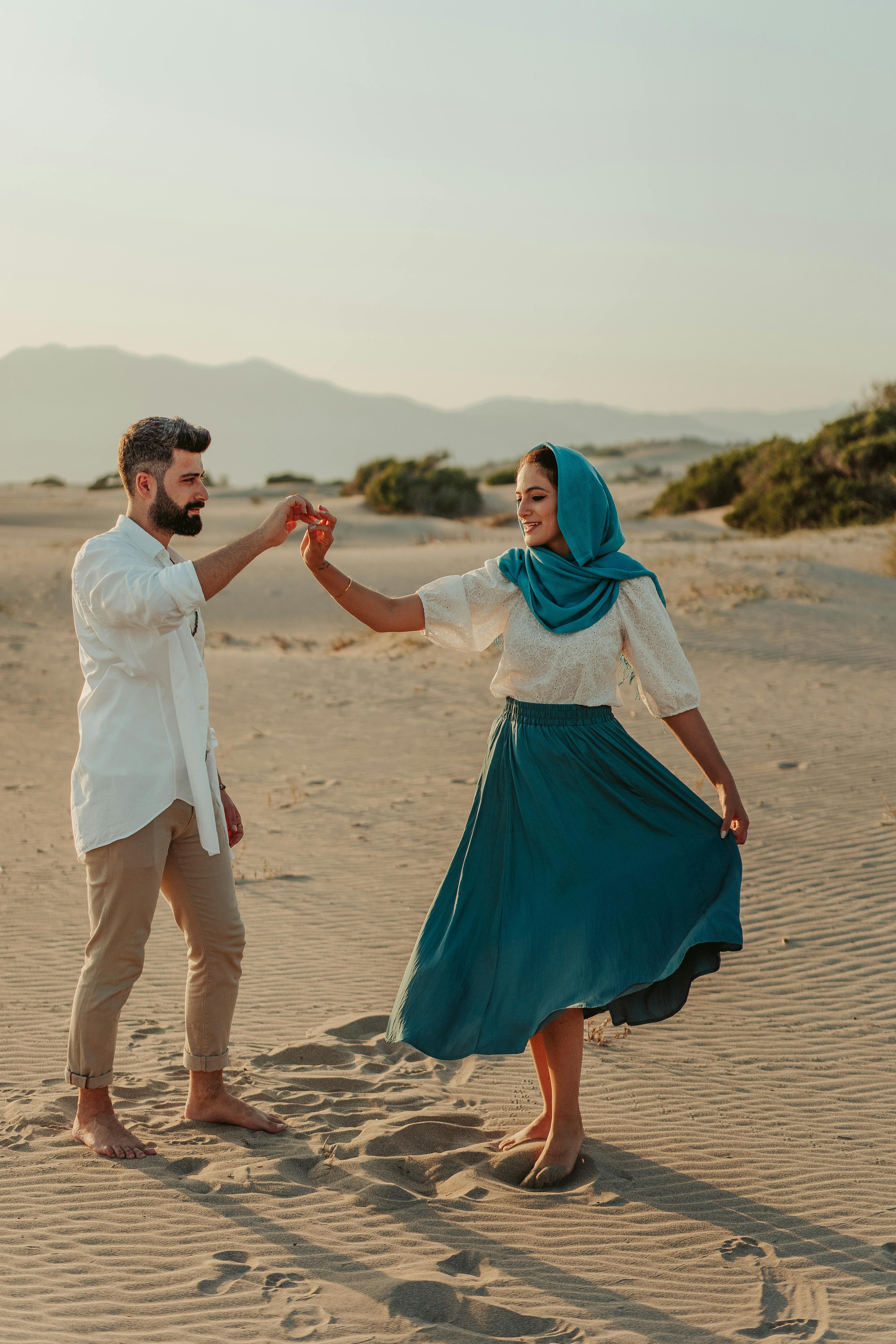 man and woman holding hands while walking on beach