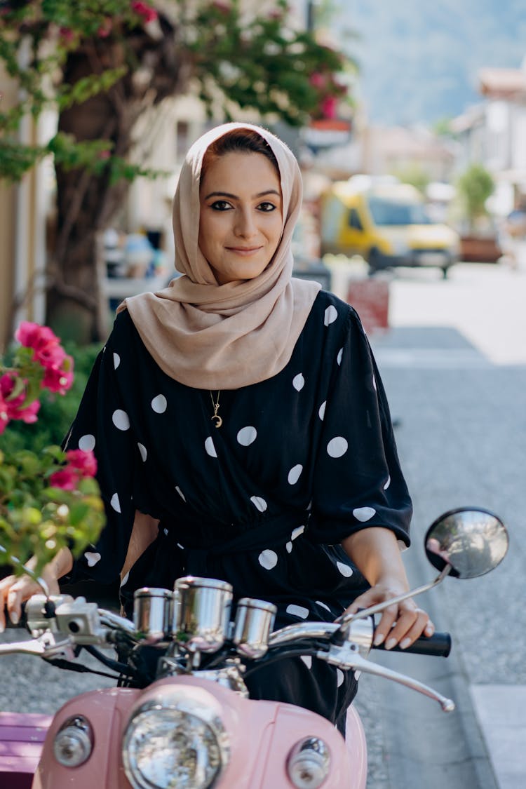 Woman In Polka Dot Dress And Hijab Riding A Pink Scooter