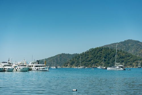 Free A serene scene of yachts anchored in a calm bay with a lush green mountain in the background. Stock Photo