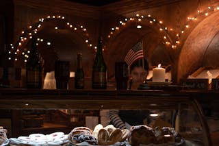 Young Woman Selling Pastries in a Room Illuminated by String Lights and Candles