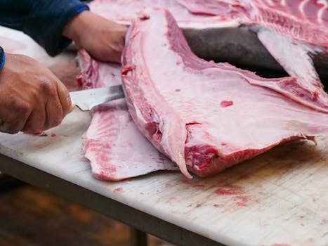 Close-up of a butcher slicing fresh tuna on a cutting board, showcasing skill and precision.