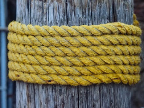 Detailed view of a thick yellow jute rope coiled around a rustic wooden post.
