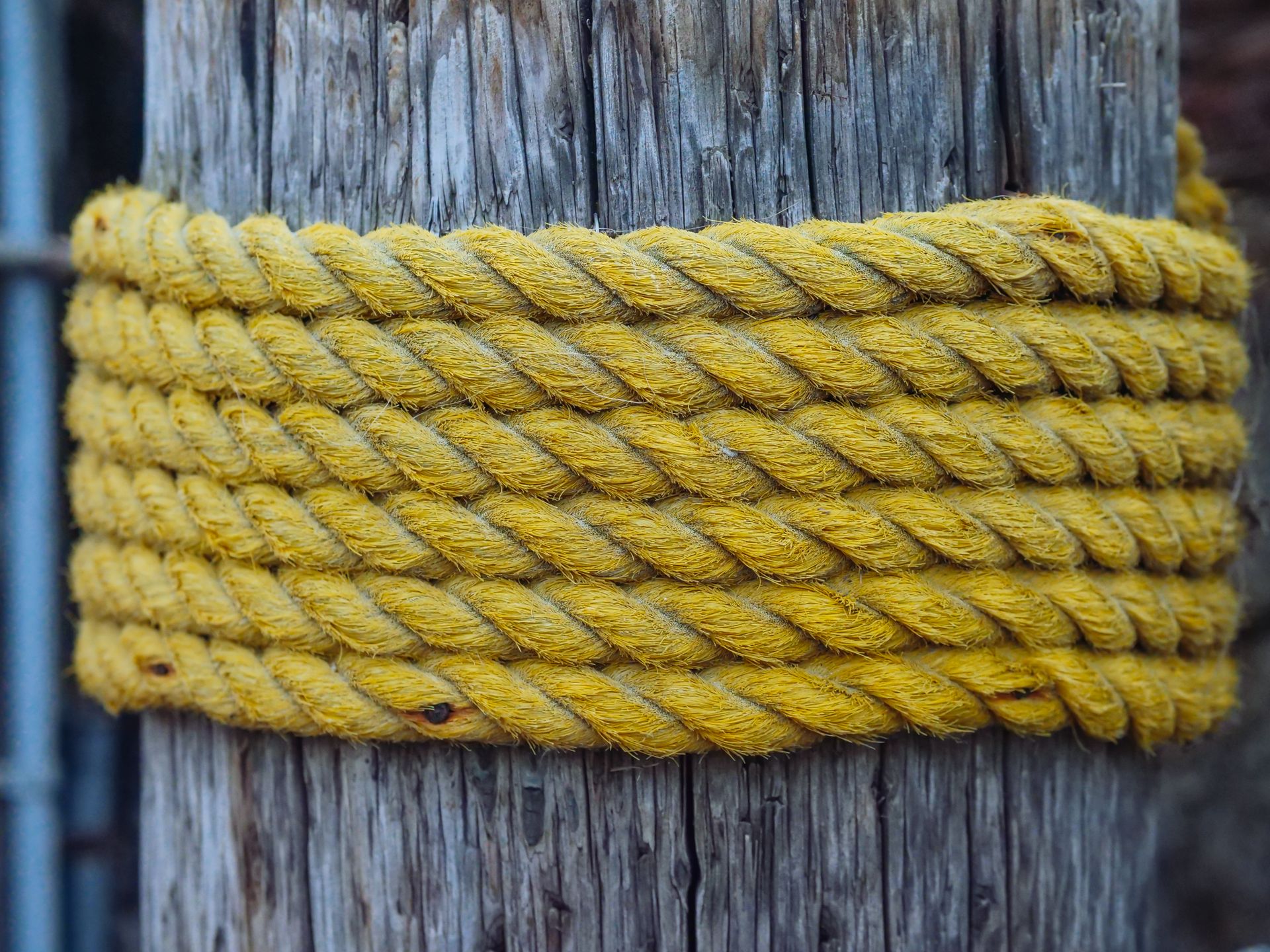 Detailed view of a thick yellow jute rope coiled around a rustic wooden post.
