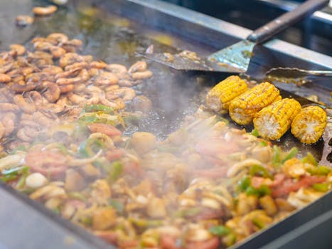 Delicious grilled prawns and corn with vegetables being cooked on a street food grill.