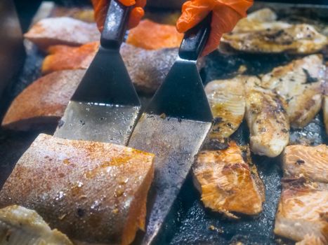 Close-up of various fish fillets being grilled with spatulas on a hot griddle, highlighting food preparation