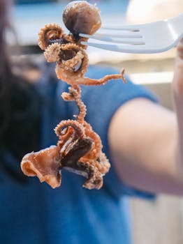 A detailed view of a grilled octopus held on a fork, ready to eat.