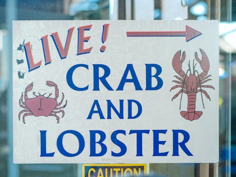 Sign advertising live crab and lobster with colorful illustrations at a seafood market.