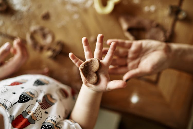 Close-up Of A Baby Holding A Gingerbread Heart Cookie On Hand 