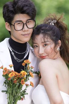 A joyful couple posing together in wedding attire, holding a bouquet with a blurred background.