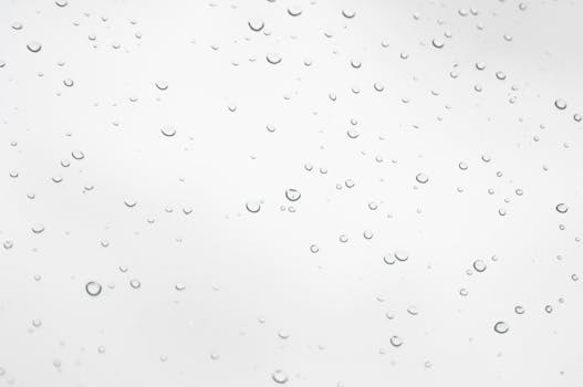 Close-up of clear water droplets scattered across a smooth white background, creating a minimalist effect.