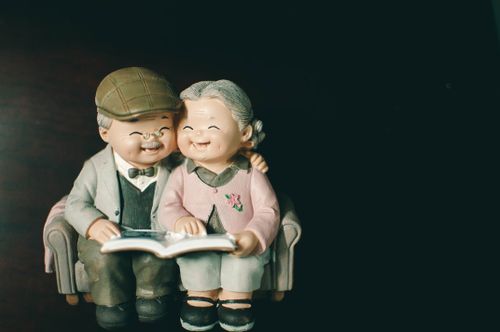 Free Cute figurines of an elderly couple sitting on a sofa and sharing a book, evoking warmth and nostalgia. Stock Photo