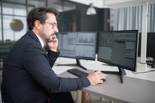 Man in Black Sitting Behind A Desk Using Cellphone