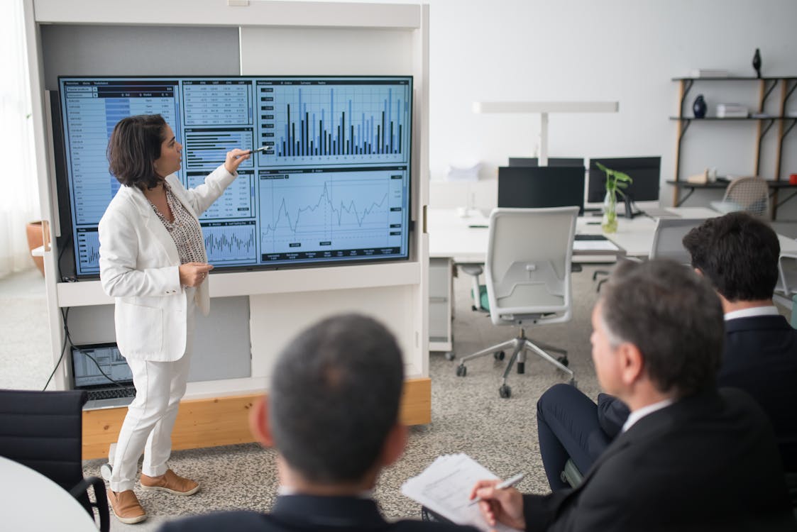 Woman in White Suit Discussing Stock Market Data To Her Colleagues