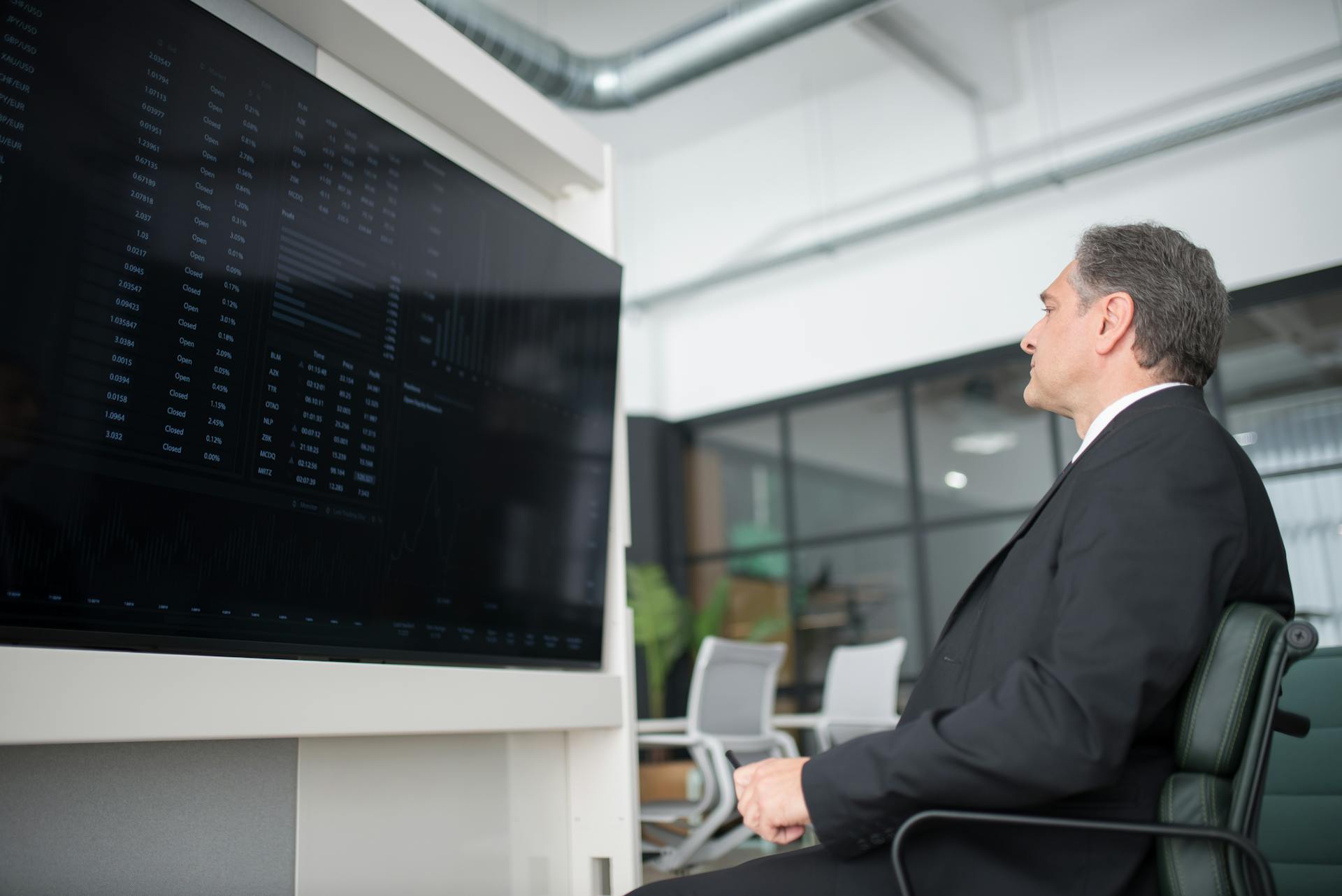 A professional businessman in a modern office analyzing stock market data on a large screen.