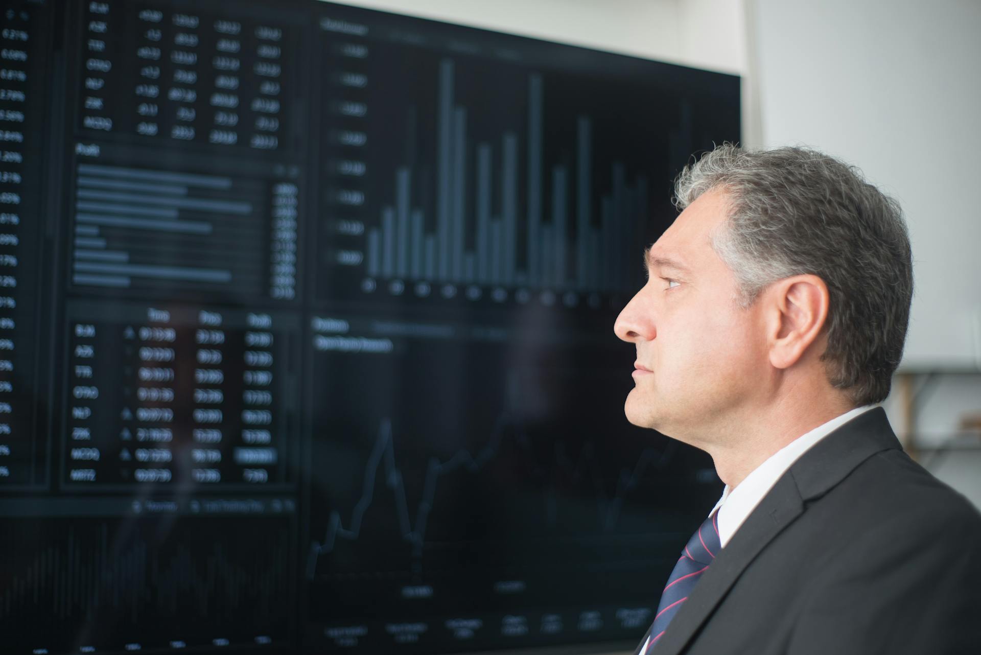 Mature businessman in corporate attire analyzing financial charts on a screen indoors.