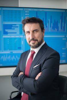 Confident businessman in suit posing in front of data screens in a modern office.
