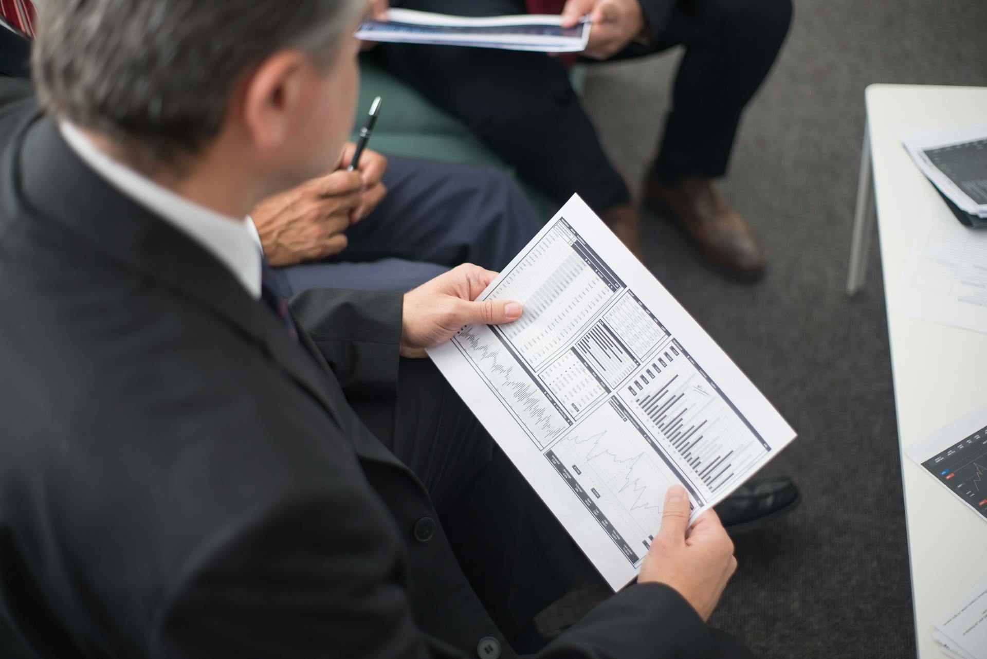 Two businessmen analyze financial documents during a meeting, focusing on data trends and performance.