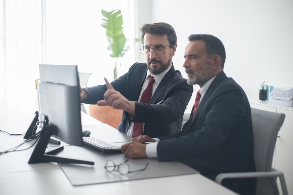 Dos colegas masculinos colaborando en un proyecto en el ordenador en una oficina moderna y luminosa.