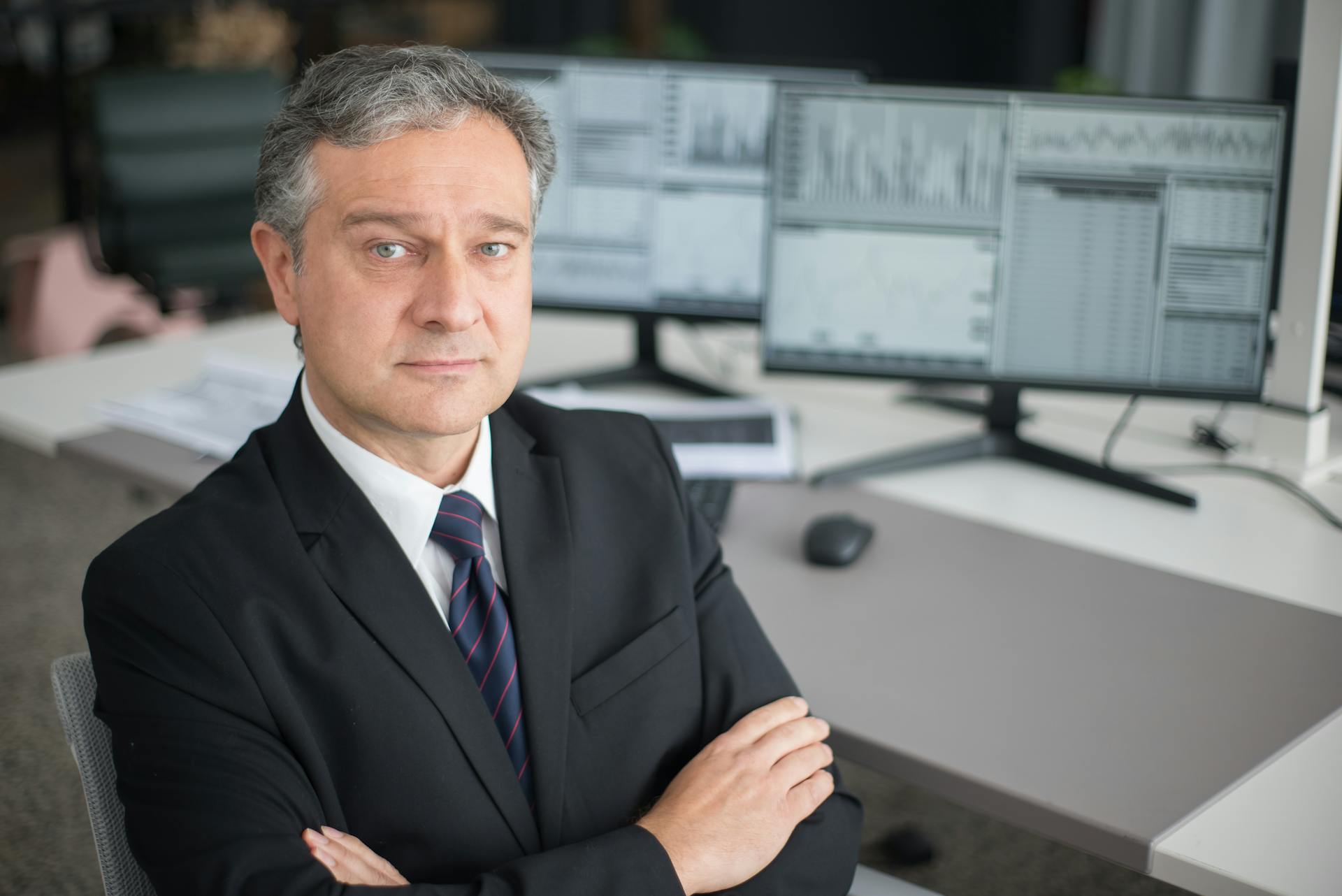 Business executive in office focused on financial analysis with computer monitors.