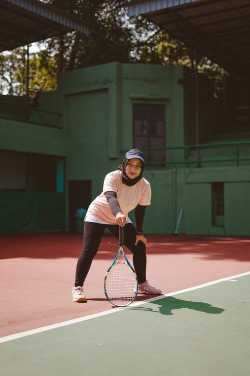 Free Focused young woman wearing hijab playing tennis on an outdoor court, showcasing strength and concentration. Stock Photo