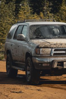 A rugged SUV covered in mud parked on a dirt road surrounded by dense forest.