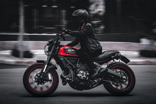 Free A rider with a black leather jacket and helmet speeds on a red motorcycle in a city. Stock Photo