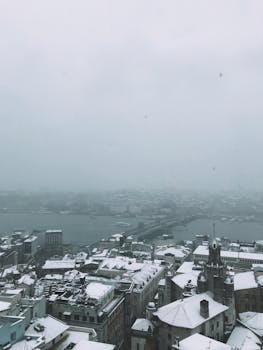 Aerial view of snow-covered Istanbul cityscape with cloudy and foggy atmosphere.