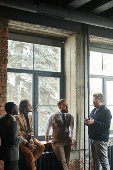 A group of diverse male professionals engaged in conversation by large windows.