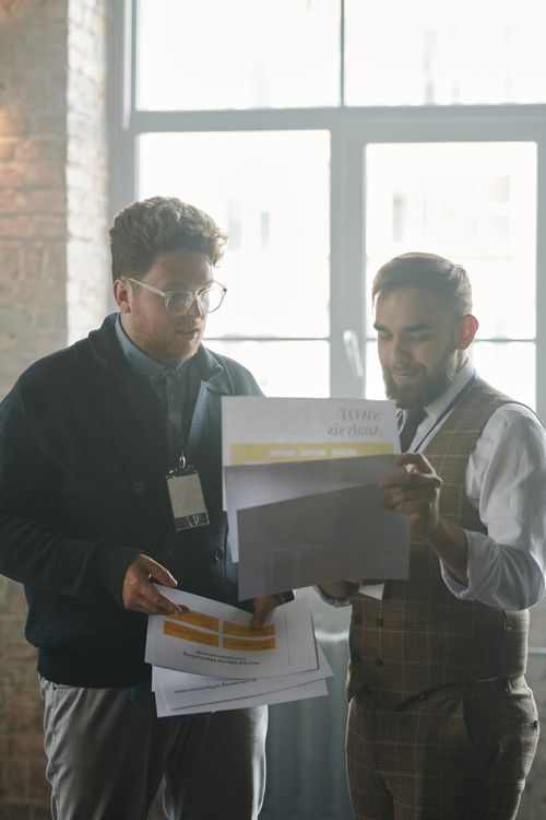 Free Two businessmen engage in a discussion, reviewing documents indoors. Stock Photo