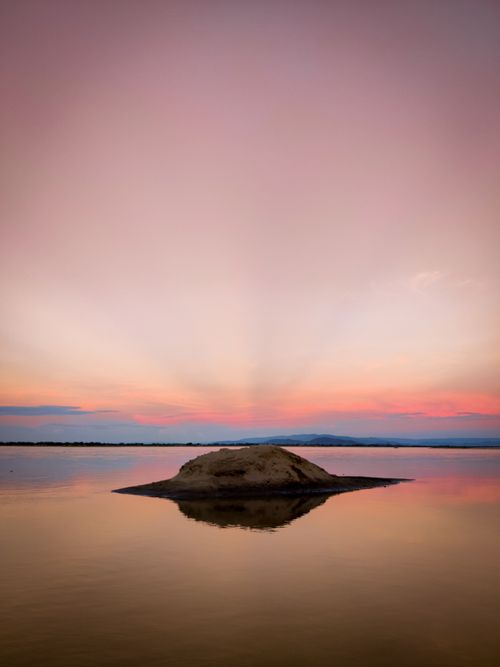 Free Tranquil ocean scene at sunset with a solitary rock in still waters and a vibrant sky. Stock Photo