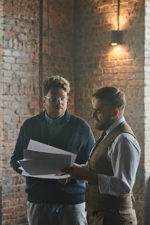 Free Two men discussing paperwork in a rustic office with exposed brick walls. Stock Photo