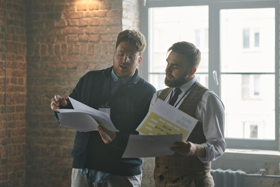 Two businessmen discussing documents in an industrial-style office setting. Two businessmen discussing documents in an industrial-style office setting.