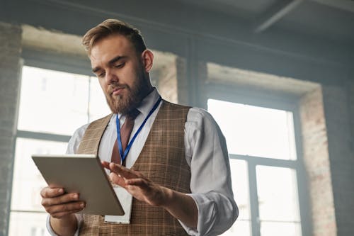 Man in White Long Sleeves and Plaid Vest Holding a Tablet Computer 