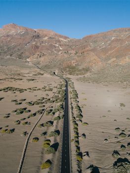 Aerial shot of a long winding road through a barren desert landscape with mountains in the background.