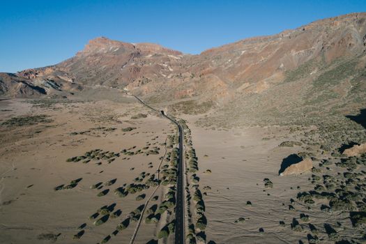 Aerial view of a narrow road winding through a rugged desert landscape with mountains and sparse vegetation.