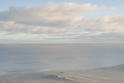 An Aerial Photography of a Beach Sand Near the Ocean Under the White Clouds and Blue Sky